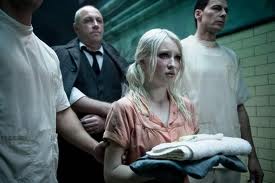 Still from Sucker Punch showing a young white blonde girl being led down an asylum corridor by male orderlies and a tall older white man in a suit
