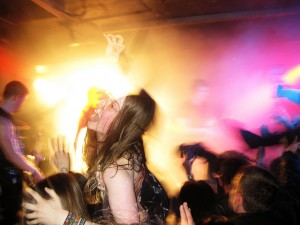 photo showing a young white woman with long light brown hair crowdsurfing at a metal gig
